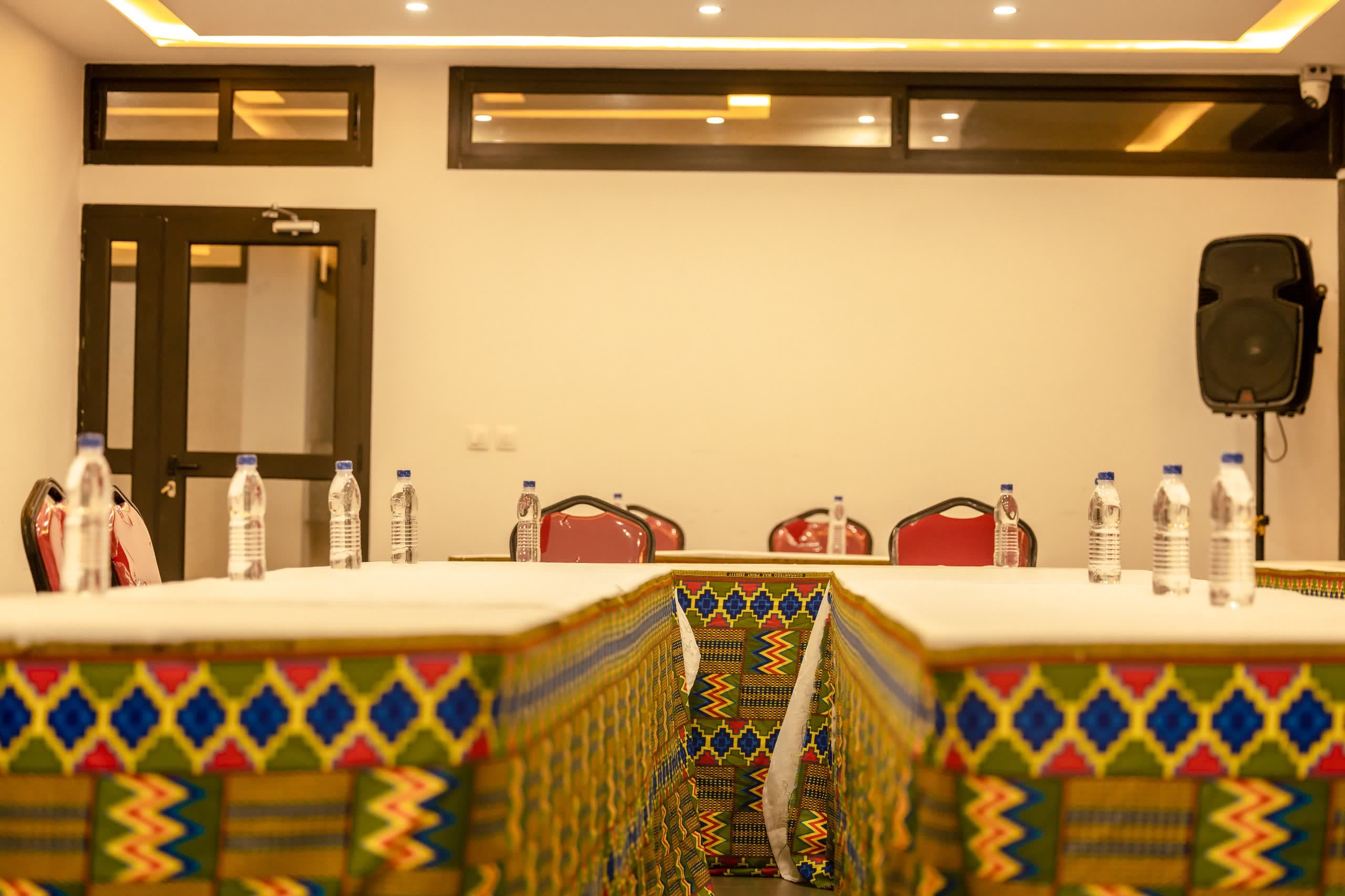 Salle de conférence de NH Le Rêve dressée en U, nappage blanc et jupes de table en pagne kente, sonorisation en place