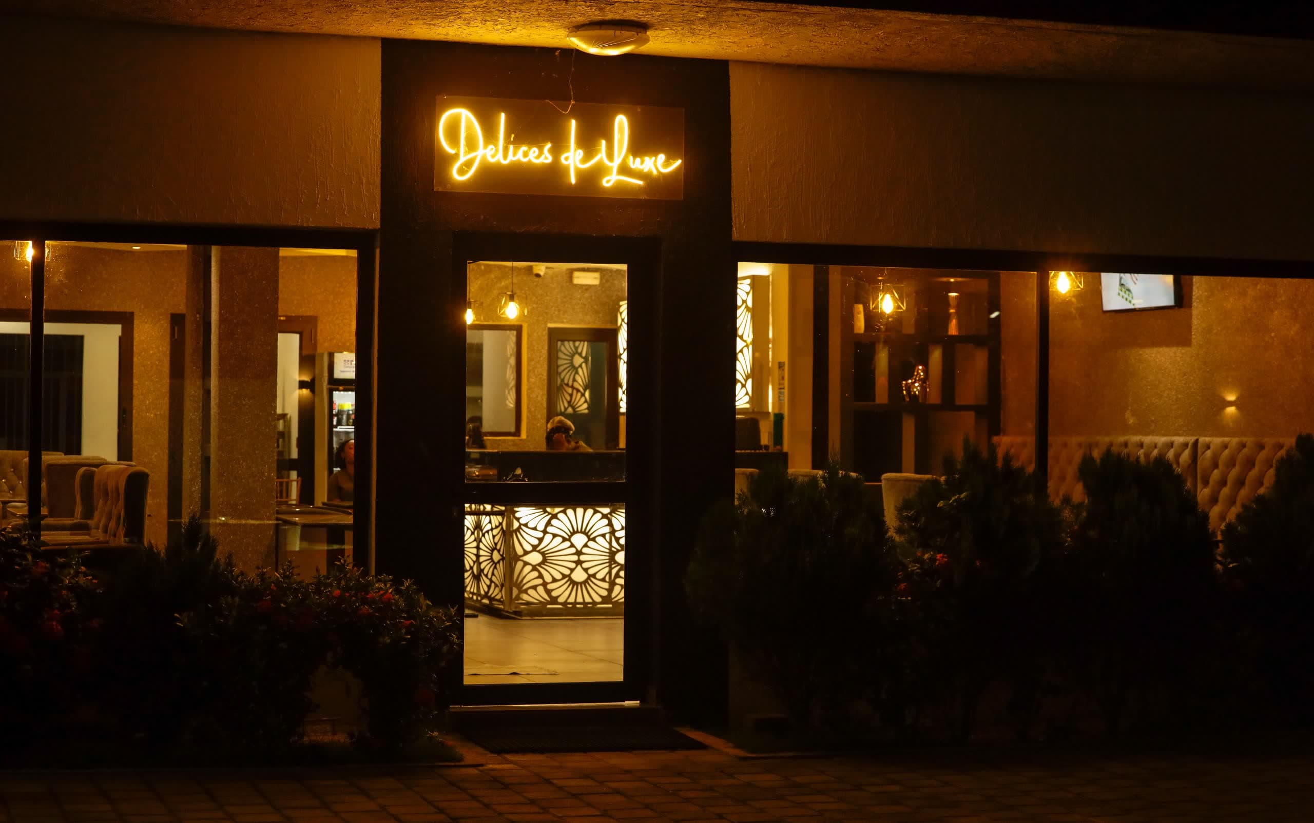 Façade du restaurant Délices de Luxe à NH Le Rêve, enseigne néon dorée de nuit